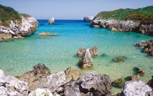 Alt: la playa de Buelna en Llanes, Asturias con marea alta y aguas cristalinas